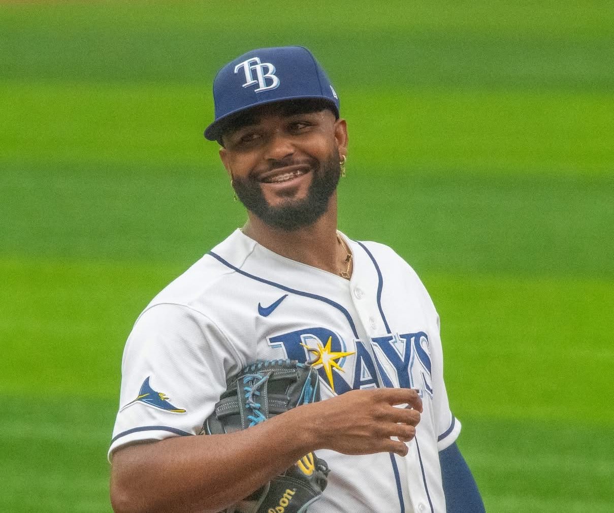 Tampa Bay Rays third baseman Junior Caminero in the Rays home white uniform and navy TB cap, smiling on the infield with his glove during a game