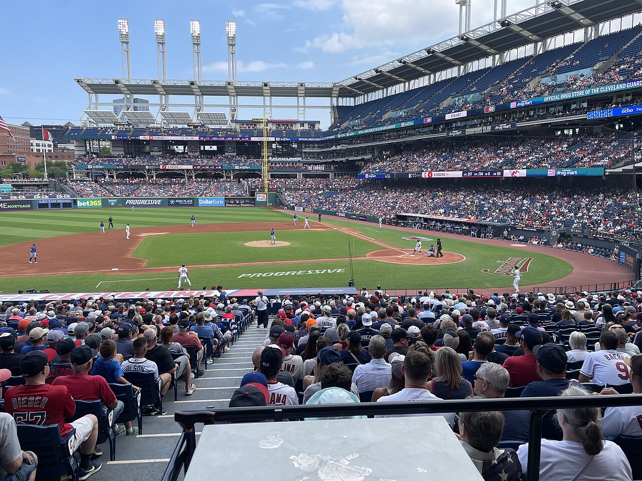 A Cleveland Guardians home game in progress at Progressive Field in August 2026, seen from the lower bowl behind first base with a packed crowd